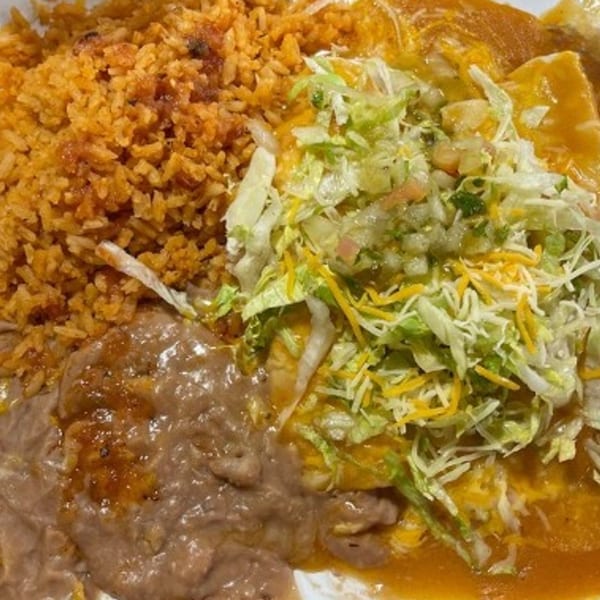 A close-up of a Mexican combo plate with rice, refried beans, and enchiladas topped with lettuce and cheese.